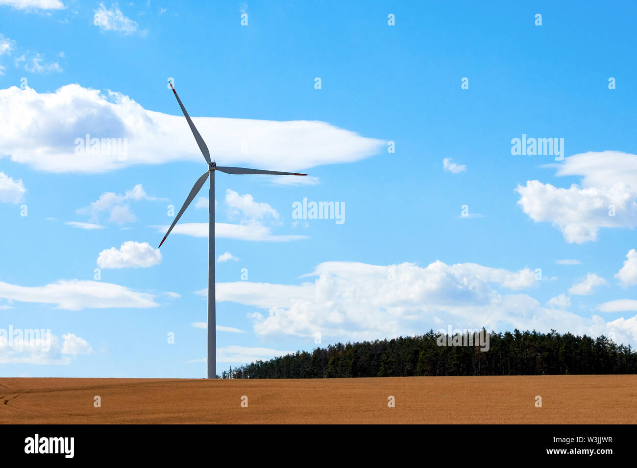 Wind power station con un polo e il mulino a vento, vicino alla foresta e cornfield nella campagna sotto il cielo blu con nuvole bianche. Foto Stock