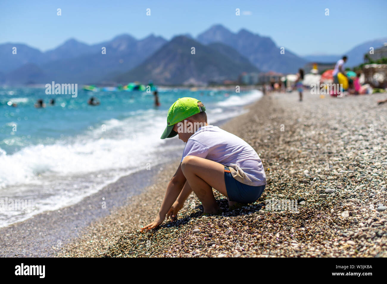 Il ragazzo sulla riva del mare blu. Per i bambini è utile per il relax sul mare. Spiaggia sul Mar Mediterraneo sullo sfondo delle montagne Foto Stock