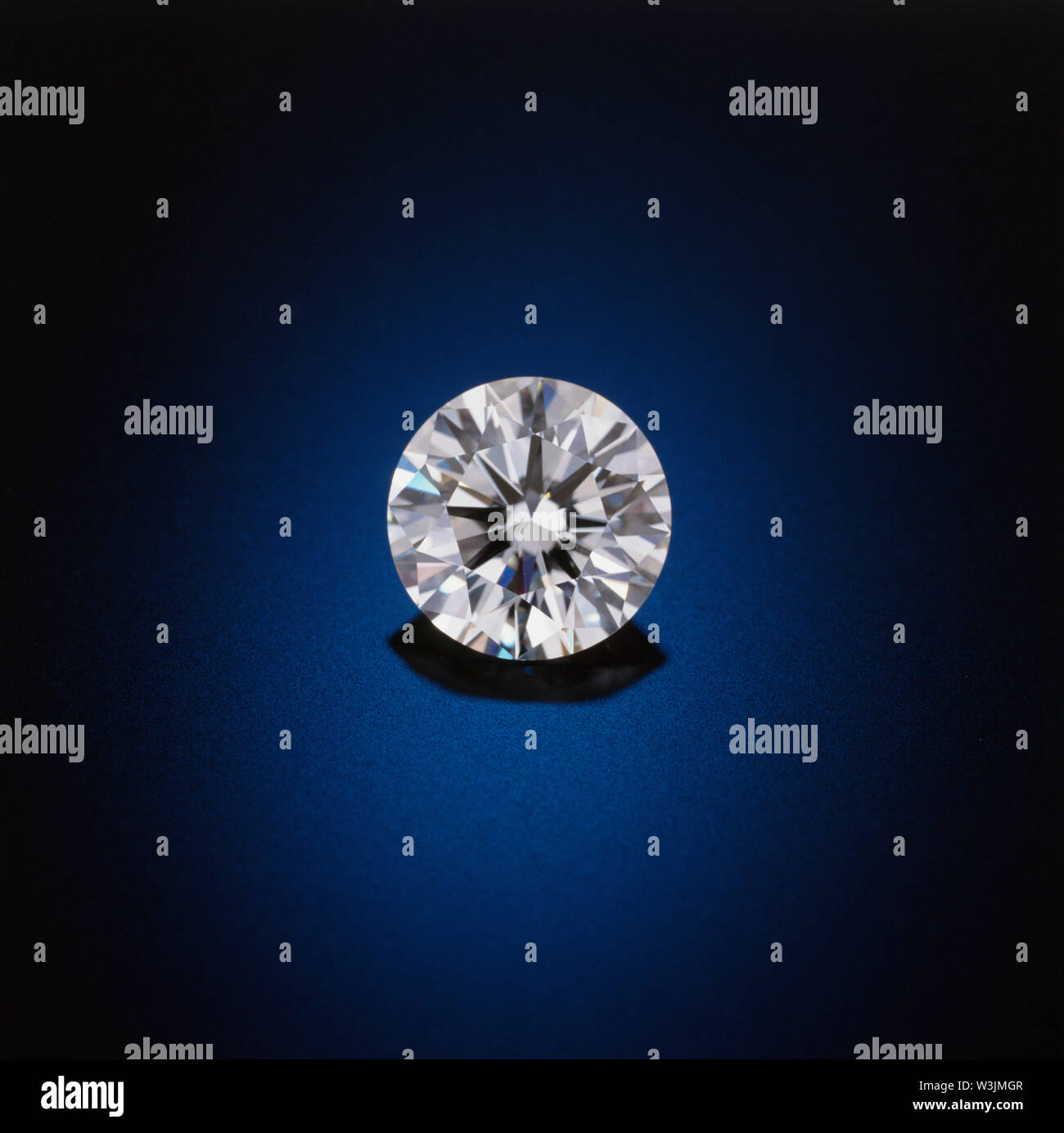 Un solitario, pulito e chiaro, sfaccettata round diamond siede su un blu riflettente, sfondo nero. Foto Stock