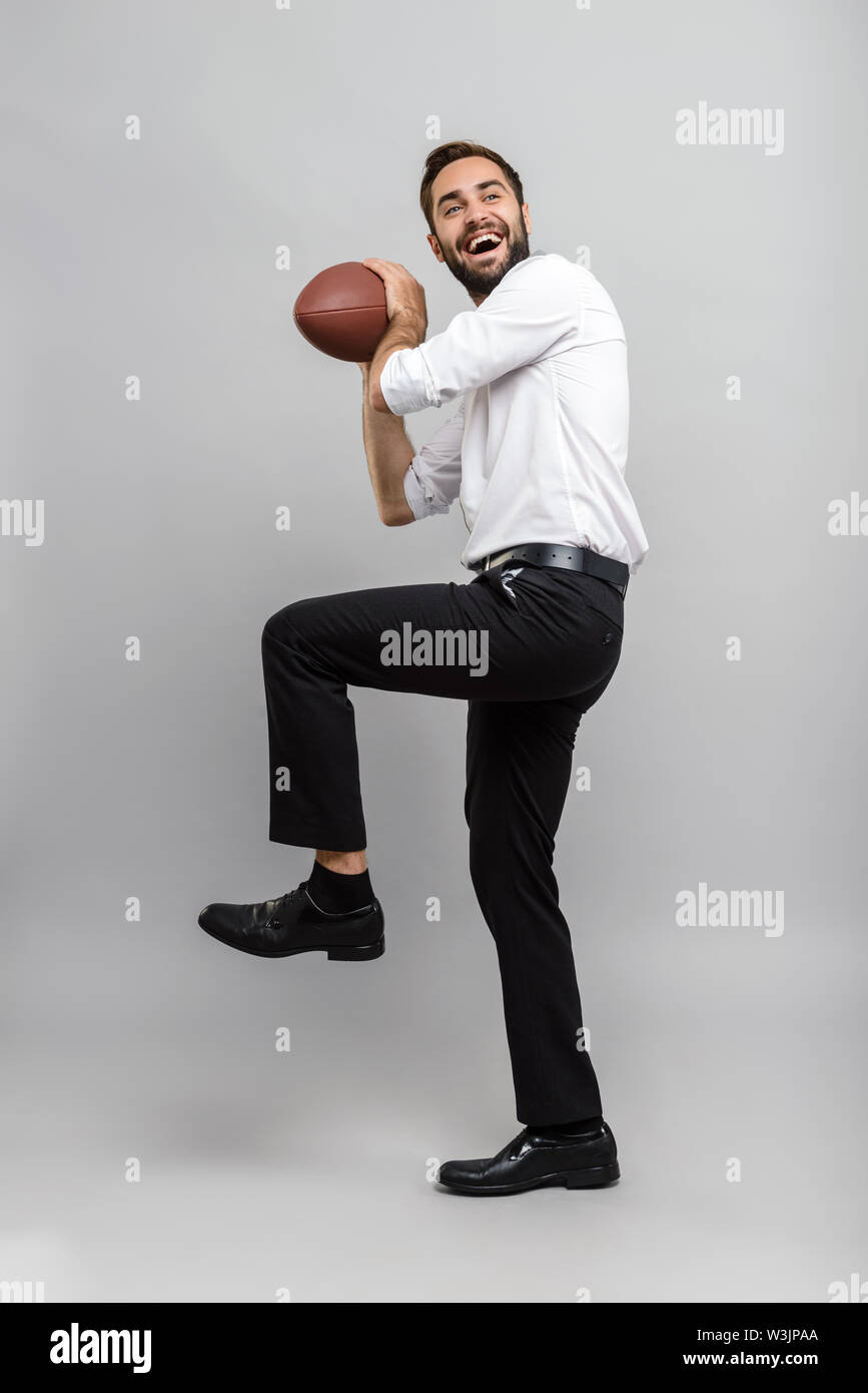 A piena lunghezza Ritratto di un bel giovane imprenditore che indossa una camicia bianca e cravatta in piedi isolate su uno sfondo grigio, tenendo palla da rugby Foto Stock