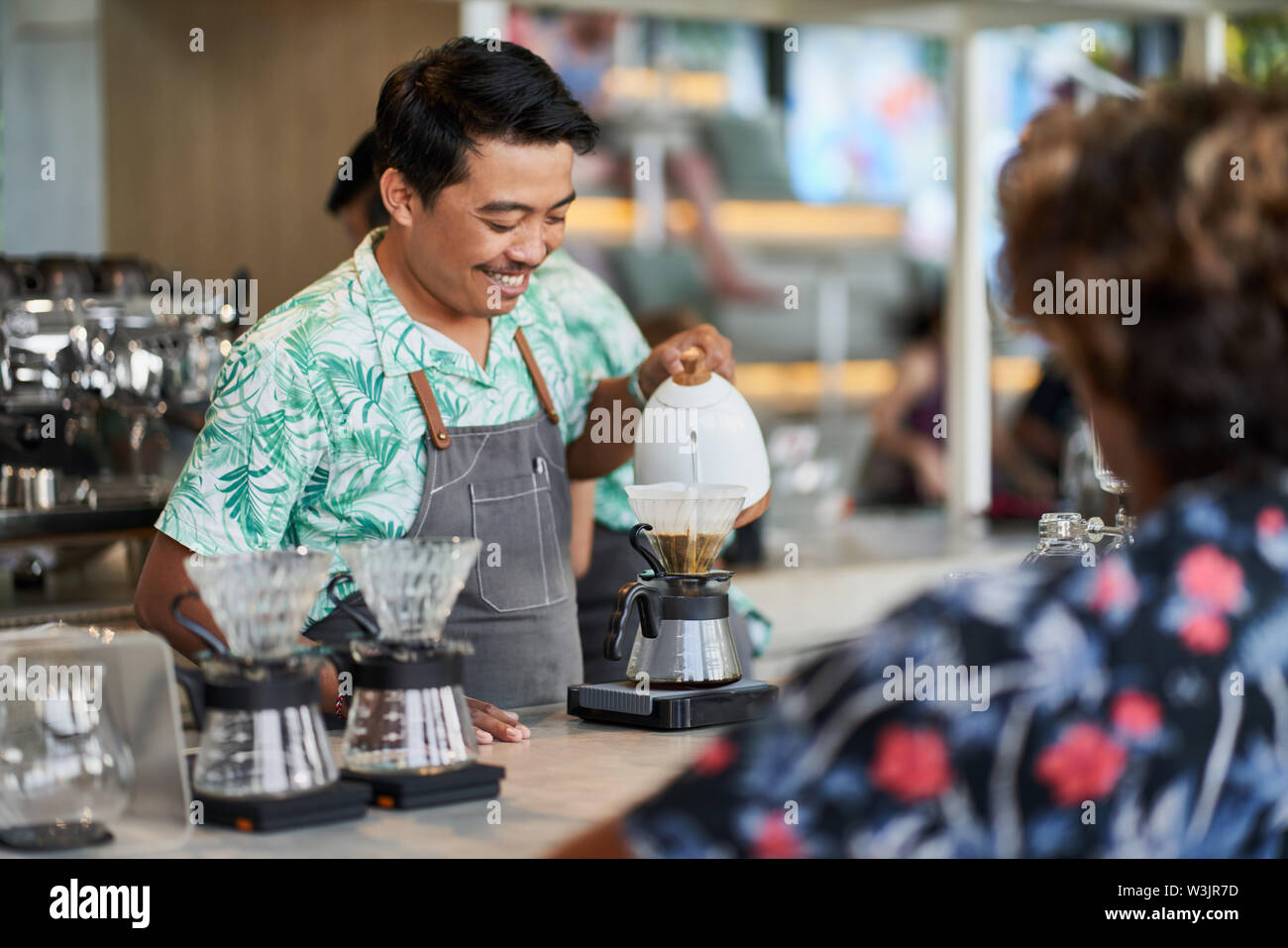 Schietto stile di vita colpo di sorridente indonesiano etnica barista e proprietario di piccola impresa la preparazione di organic fair-trade caffè nella luminosa trendy coffee shop Foto Stock