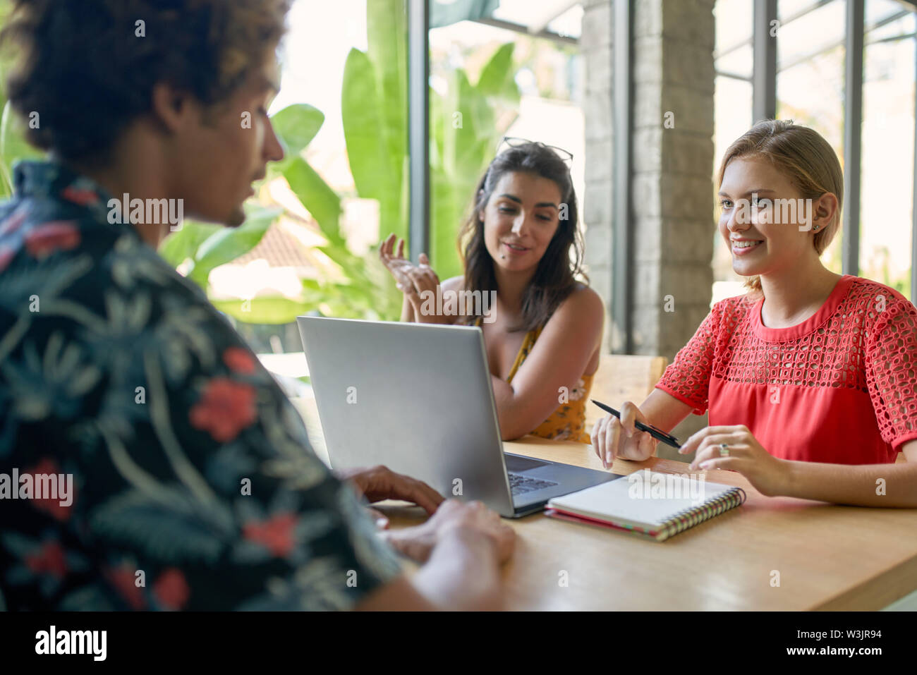 Schietto stile di vita colpo di tre diversi amici millenario lavorando insieme sul computer portatile in luminosi e moderni cafe Foto Stock