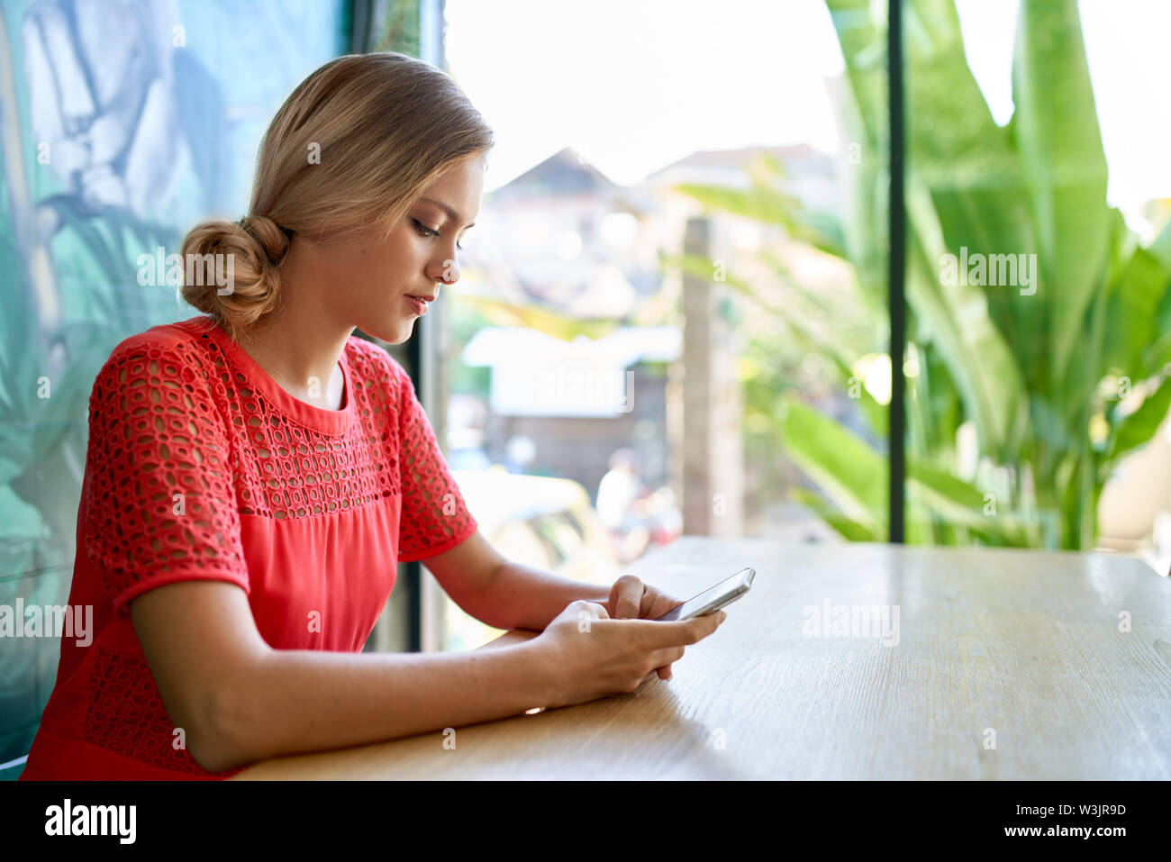 Colpo di stile di vita dei giovani caucasici bionda naturale donna millenario lavoro su cellulare a un moderno tropicale e luminoso ufficio con le piante Foto Stock