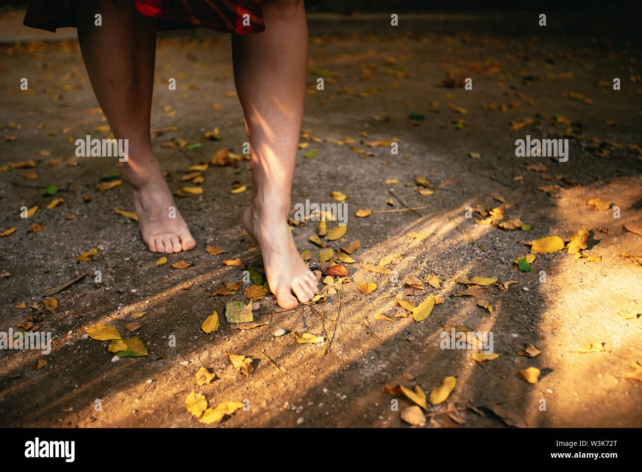 Giovane donna correre a piedi nudi attraverso foglie di autunno su un sentiero nella La Concepción Historical-Botanical giardino, Malaga, Spagna Foto Stock