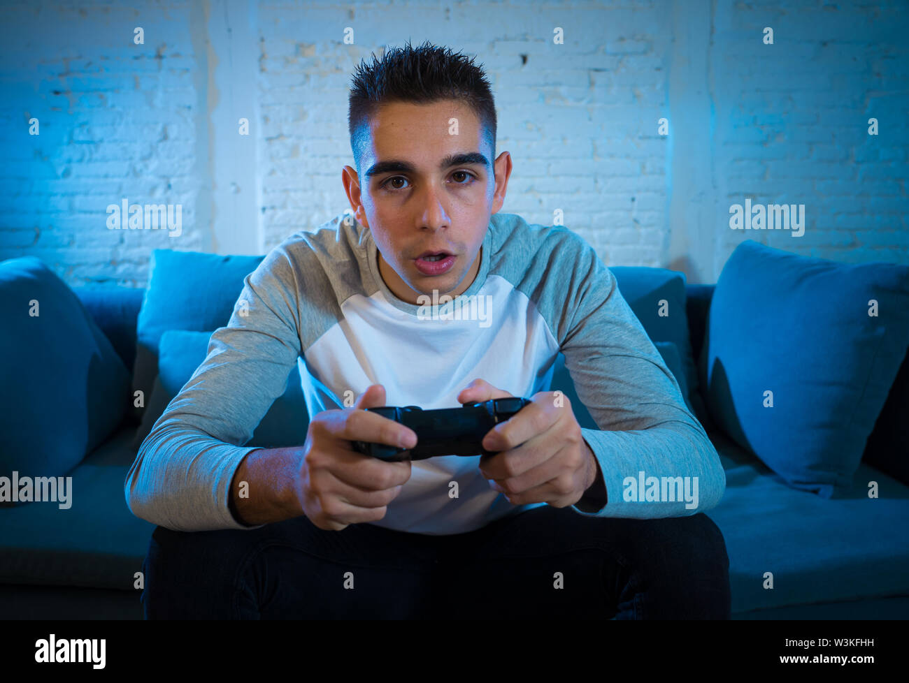 Ritratto di giovane studente uomo per giocare con i videogiochi di notte utilizzando il telecomando wireless joystick con freak intensa addicted faccia avendo divertimento nel gioco maschio aggiungere Foto Stock
