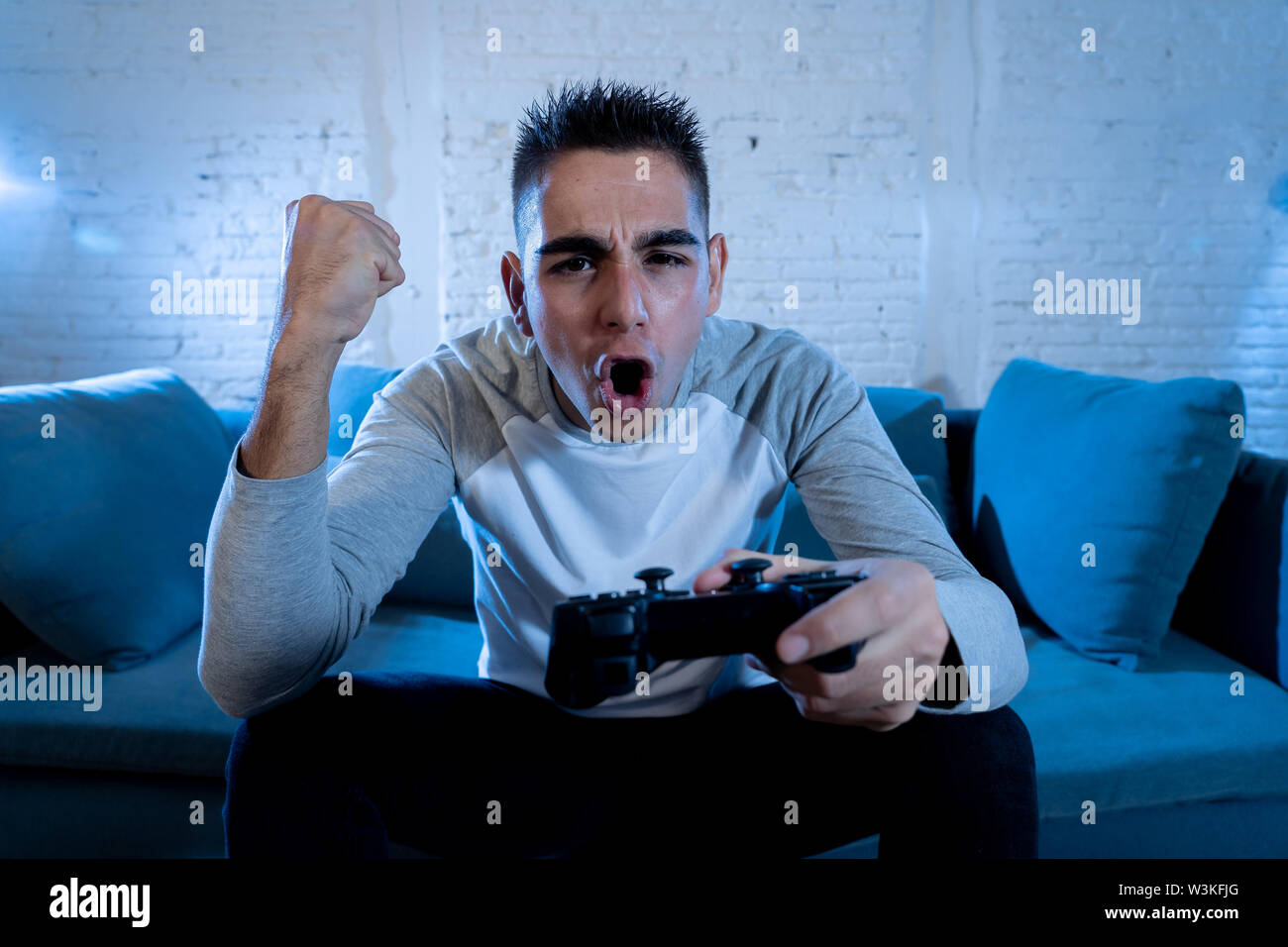 Ritratto di giovane uomo divertirsi giocando i giochi video utilizzando il telecomando wireless joystick con freak intensa faccia felice celebrare la vittoria. In gioco maschio annuncio Foto Stock