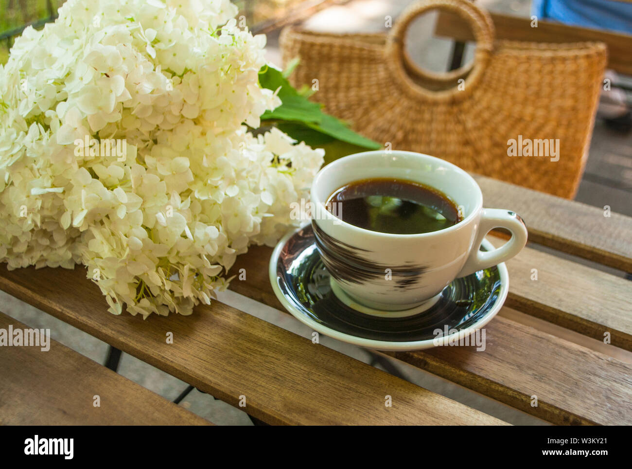 Una tazza di caffè nero su un tavolo in legno e un sacco di paglia con fiori hydragea sullo sfondo. Foto Stock