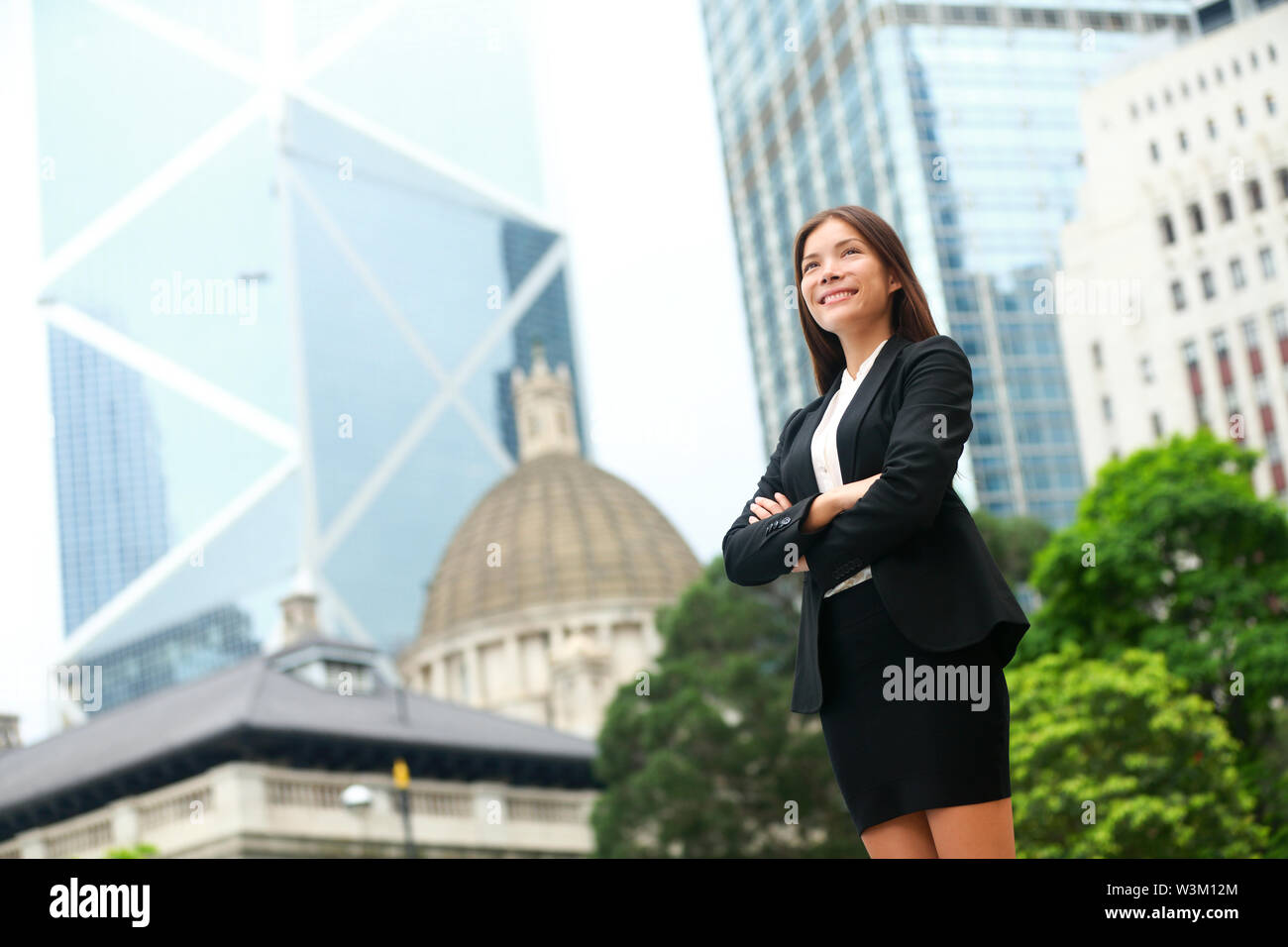 Business donna fiduciosi all'aperto in Hong Kong sta eretta in tuta cross-armati nel quartiere degli affari. Giovani multi-etnico asiatico Cinese / caucasico professionale femminile in centro a Hong Kong. Foto Stock