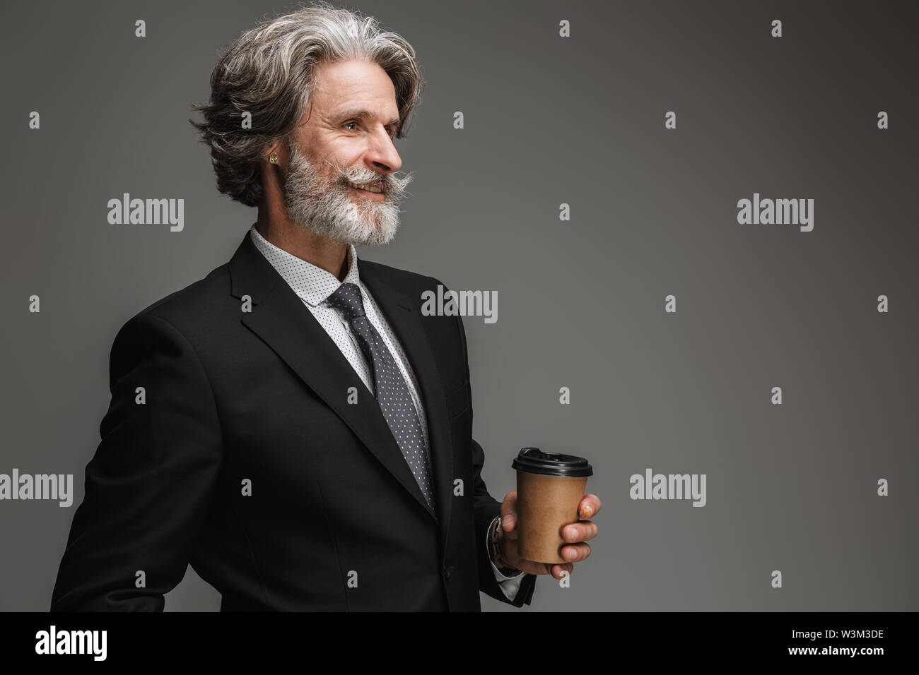 Immagine di mezza età professore uomo formale da indossare tuta nera e sorridente holding bicchiere di carta isolate su uno sfondo grigio Foto Stock