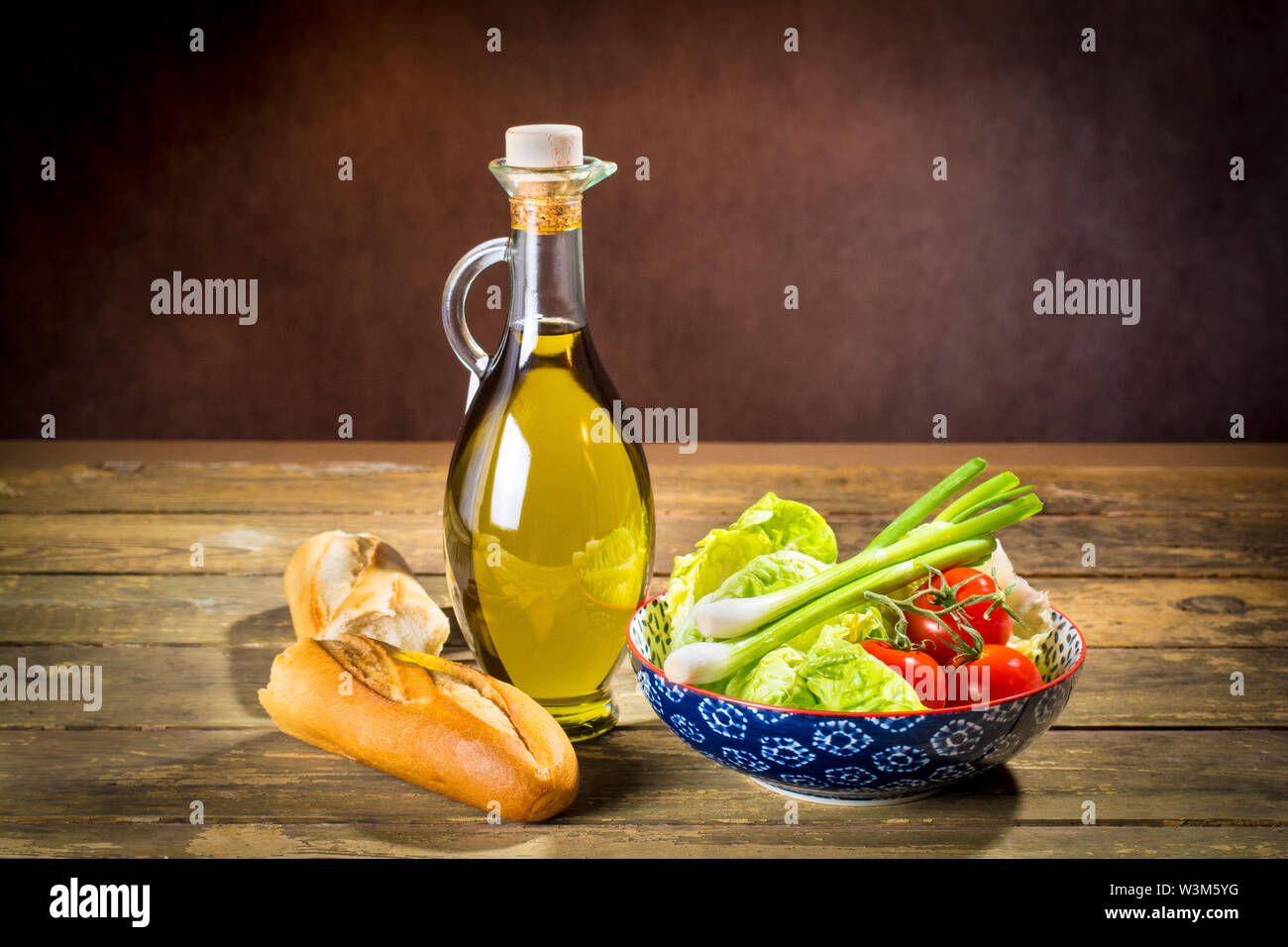 Premier qualità olio extra vergine di oliva da Jaen, Spagna, in un pallone decorativo con la stoffa di un misto di insalatiera e una baguette di pane Foto Stock