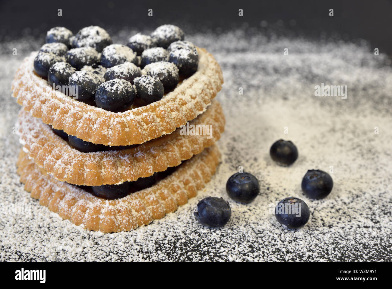 Tortine di cuori e i mirtilli con lo zucchero in polvere su di un piatto di scuro Foto Stock