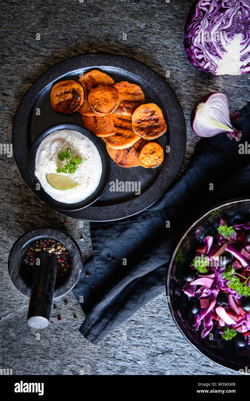 Dolce fritto fette di patate servita con panna acida dip, olive nere e insalata di cavolo rosso, cipolla rossa e barbabietole Foto Stock