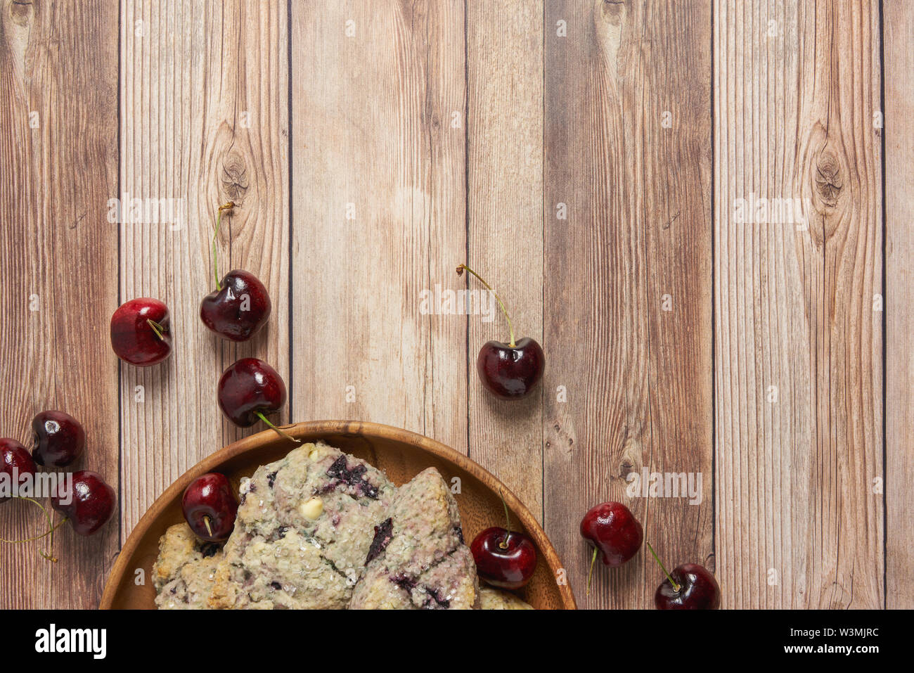Confine con piastra in legno di ciliegio e il cioccolato bianco scones su un tavolo di legno sfondo con ciliegie fresche Foto Stock