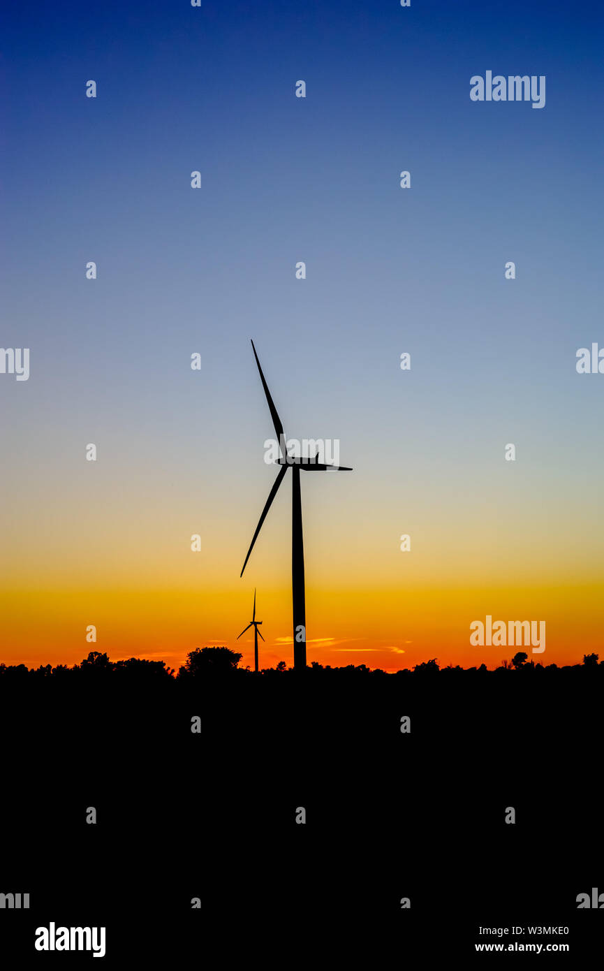 Silhouette nera di turbine eoliche contro il blu e il cielo arancione al tramonto. Foto Stock