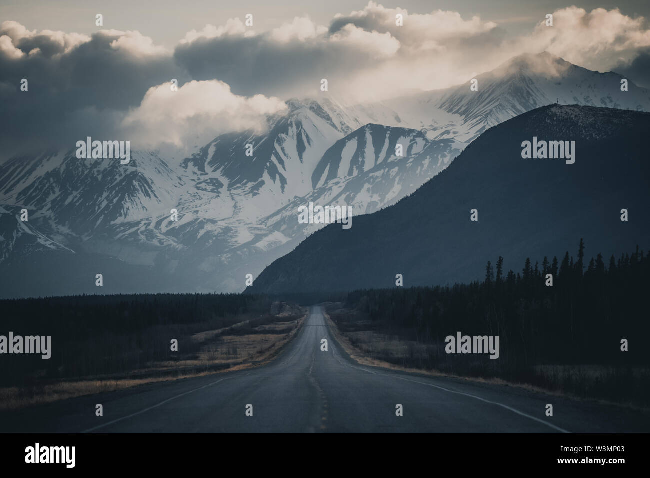 Una infinita strada che conduce alla montagna, mentre nuvole temporalesche forma nel cielo. Yukon Territory, Canada Foto Stock
