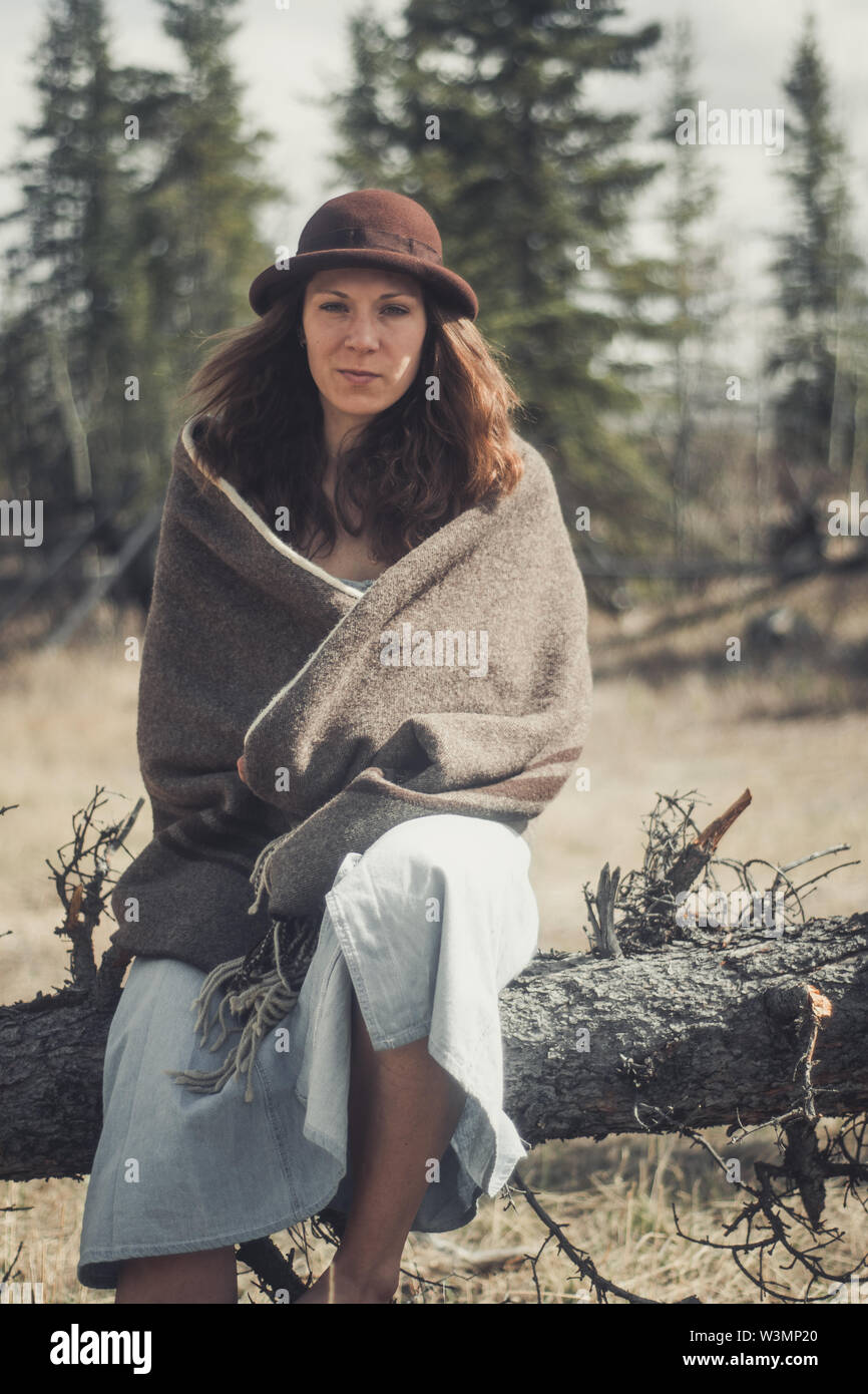 Un attraente giovane donna siede su un log avvolto in una coperta di lana. Yukon Territory, Canada Foto Stock