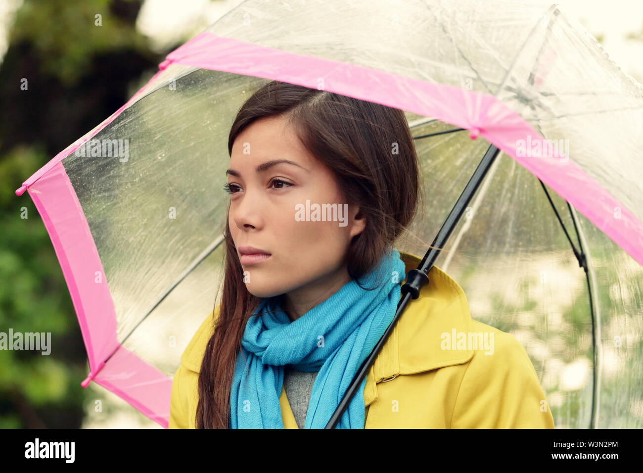 Melanconia - malinconica donna in pioggia sotto umbrelly cercando triste infelice e intelligentemente. Bella ragazza camminare sotto un ombrello trasparente sulla caduta piovosa giornata d'autunno. Multirazziale femminile nel suo 20s. Foto Stock