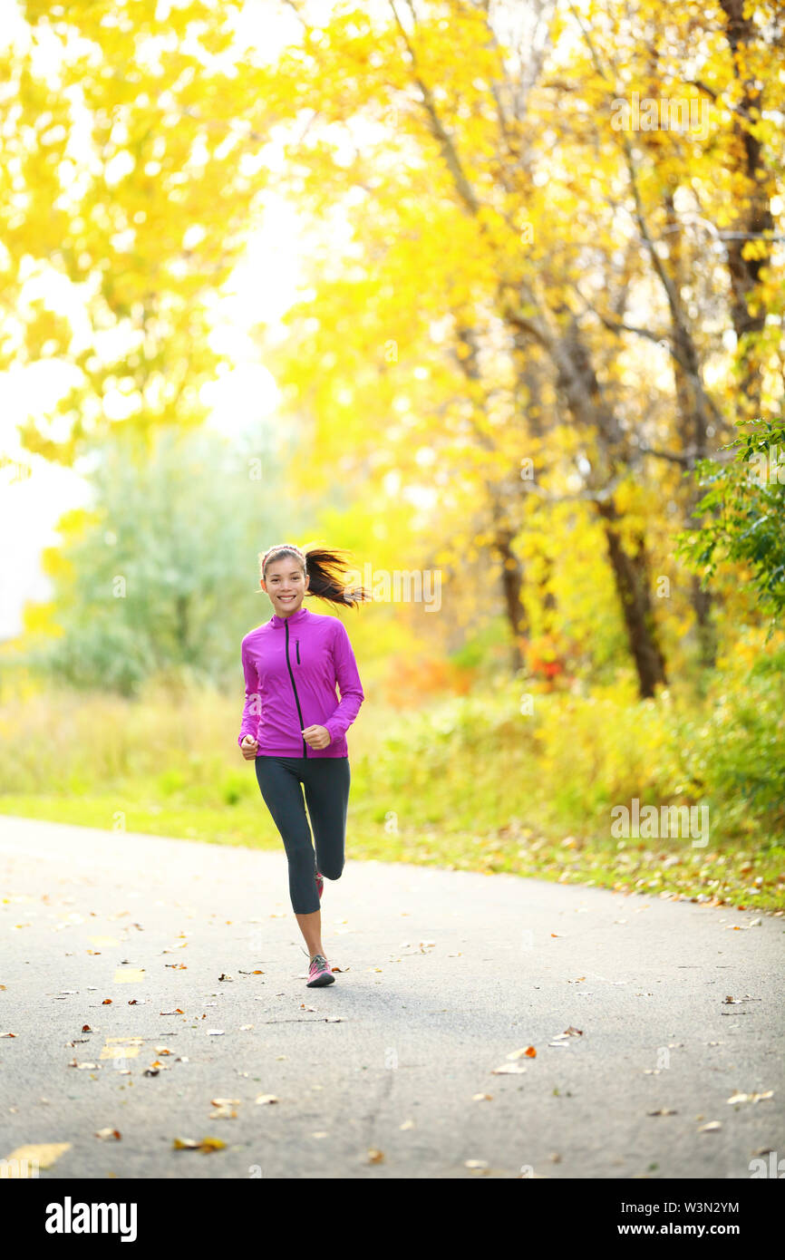 Lo stile di vita di autunno donna in esecuzione nella foresta di caduta con belle foglie gialle fogliame. A piena lunghezza Ritratto di runner jogging all'aperto sulla strada forestale. Razza mista asiatica ragazza caucasica nel suo 20s. Foto Stock