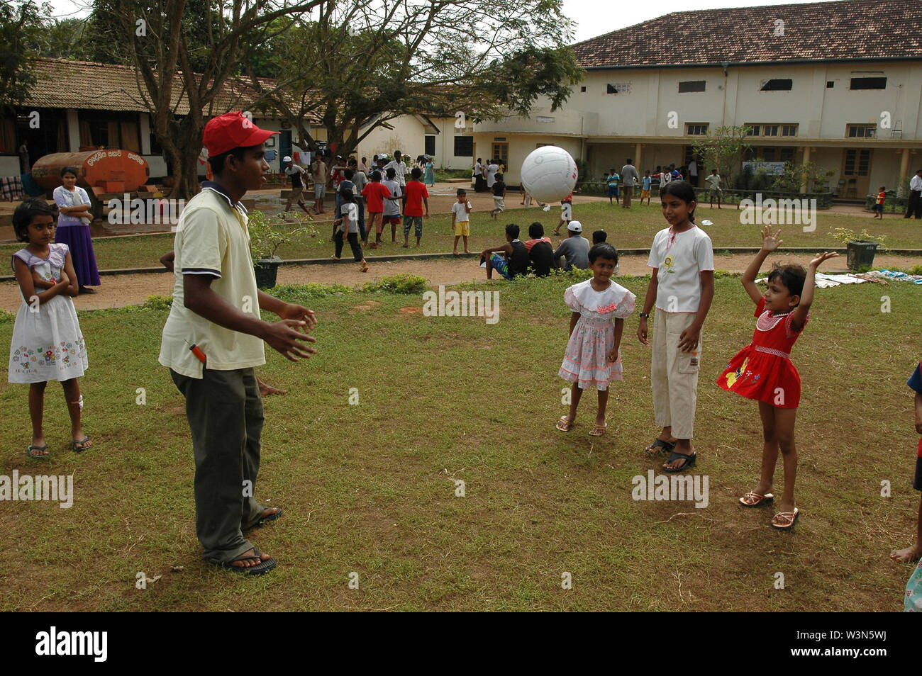 Volunteer aiuta i bambini a giocare a pallavolo in un sollievo temporaneo camp che fornisce un riparo per le famiglie che hanno perso le loro case per lo tsunami, in Thomas College nella città di Matara nel sud dello Sri Lanka. Foto Stock