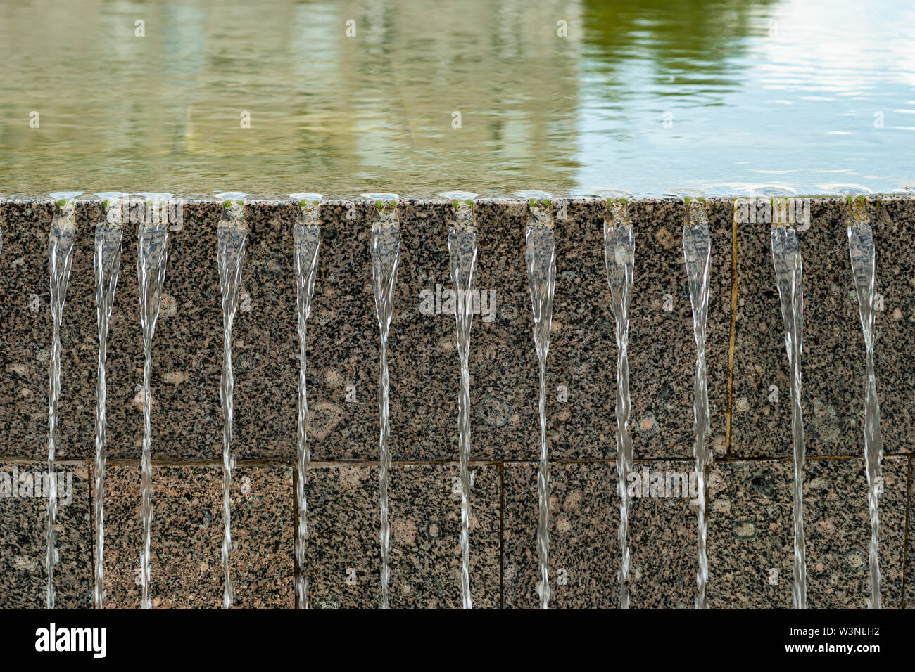 Getti di acqua di passare sopra i blocchi di granito di una fontana. Il contrasto di acqua dolce e dura pietra rock Foto Stock