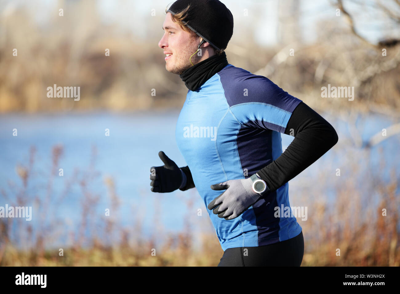 Runner uomo in autunno in esecuzione in autunno indossando i guanti e hat ascoltando musica in cuffia. Montare atleta maschio di formazione al di fuori in condizioni climatiche fredde in guide caldo capo d'abbigliamento. Modello di fitness. Foto Stock