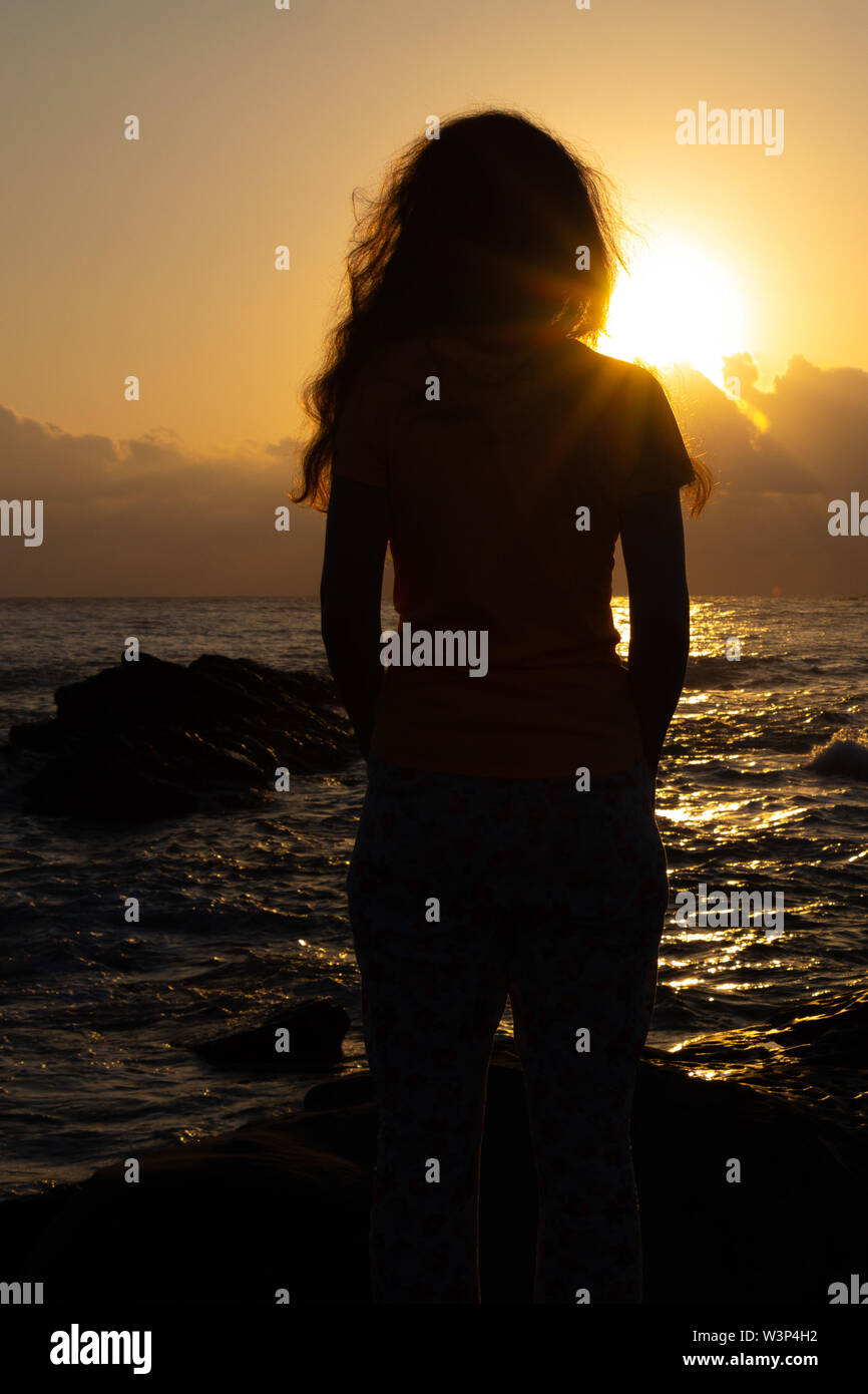 Curly ragazza guarda sunrise dall'oceano Foto Stock