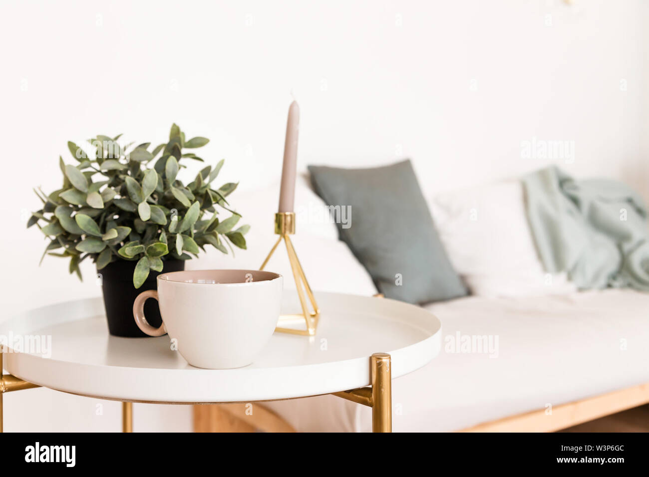 L'interno della sala in stile scandinavo. Una tazza di caffè sul tavolino accanto alle candele e una pianta in vaso Foto Stock