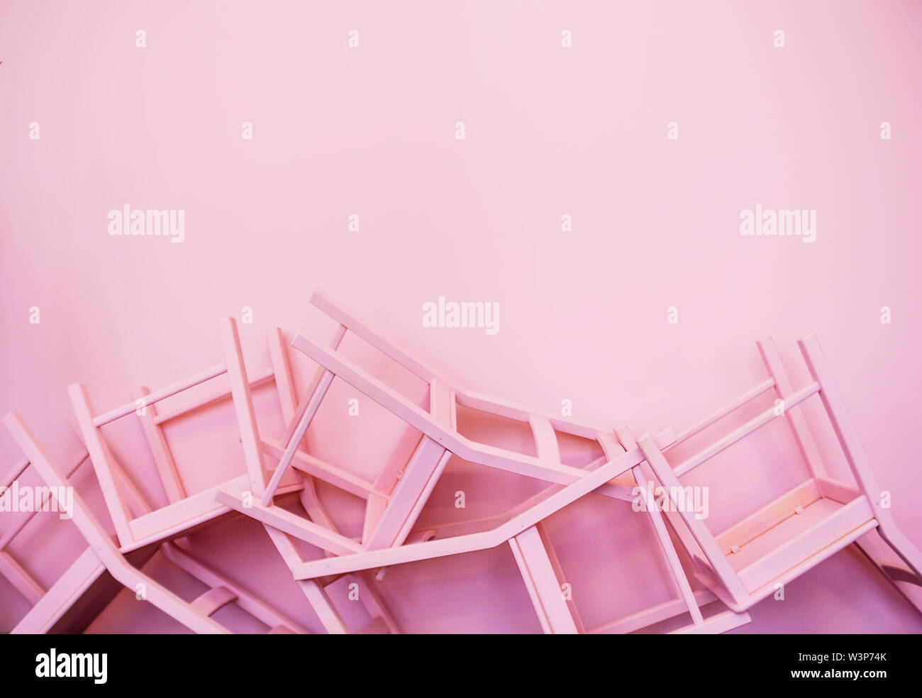 Molte sedie rosa capovolto contro lo sfondo di una parete rosa Foto Stock