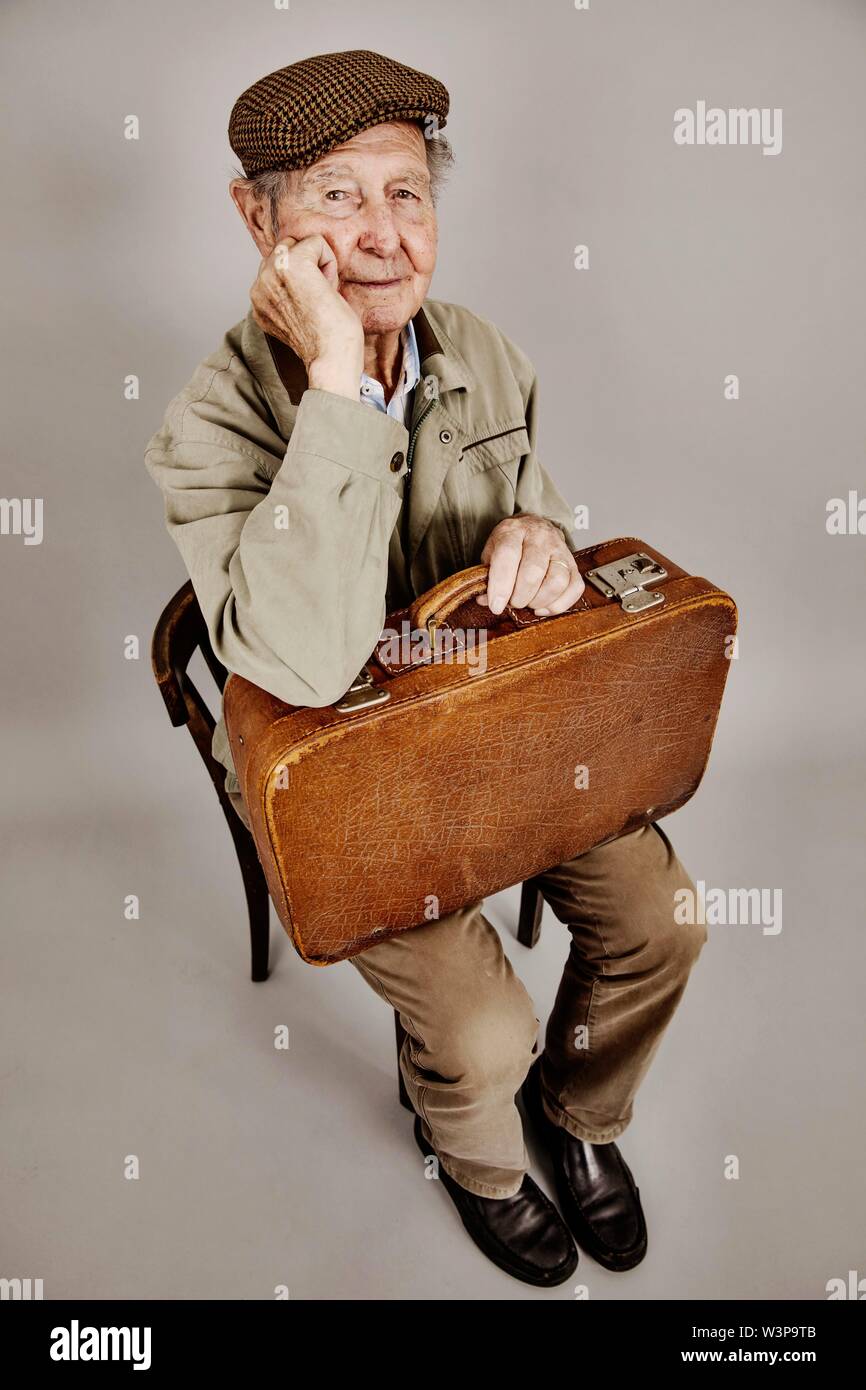 Senior si siede con la vecchia valigia su una sedia, immagine simbolica lasciando, desiderio, studio shot, Germania Foto Stock