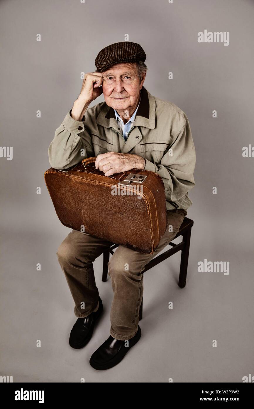 Senior si siede con la vecchia valigia su una sedia, immagine simbolica lasciando, desiderio, studio shot, Germania Foto Stock