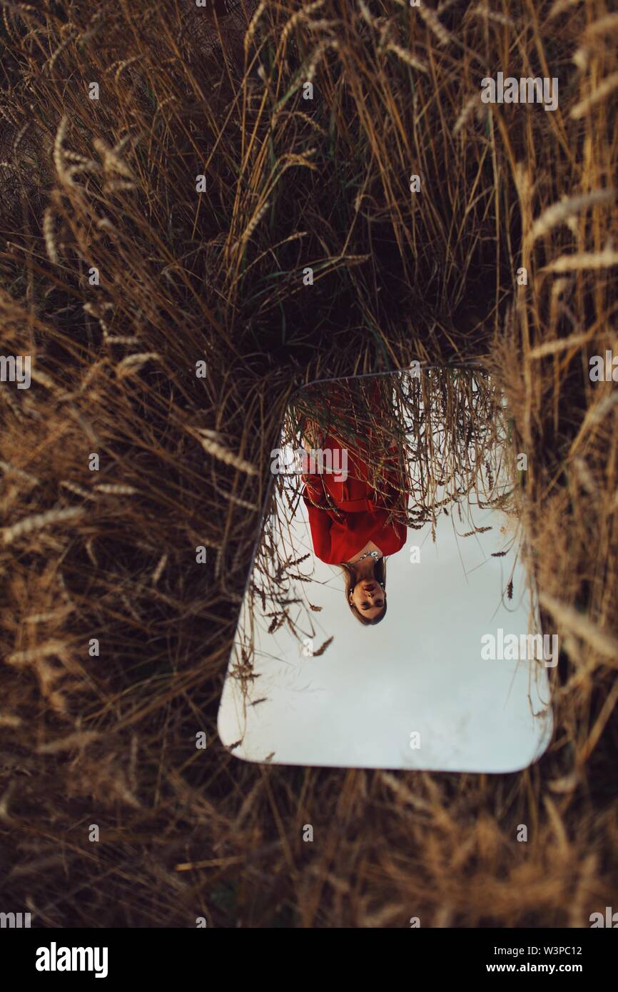 Bella donna in abito rosso nello specchio di riflessione nel campo di grano. Colpo di moda. Foto Stock