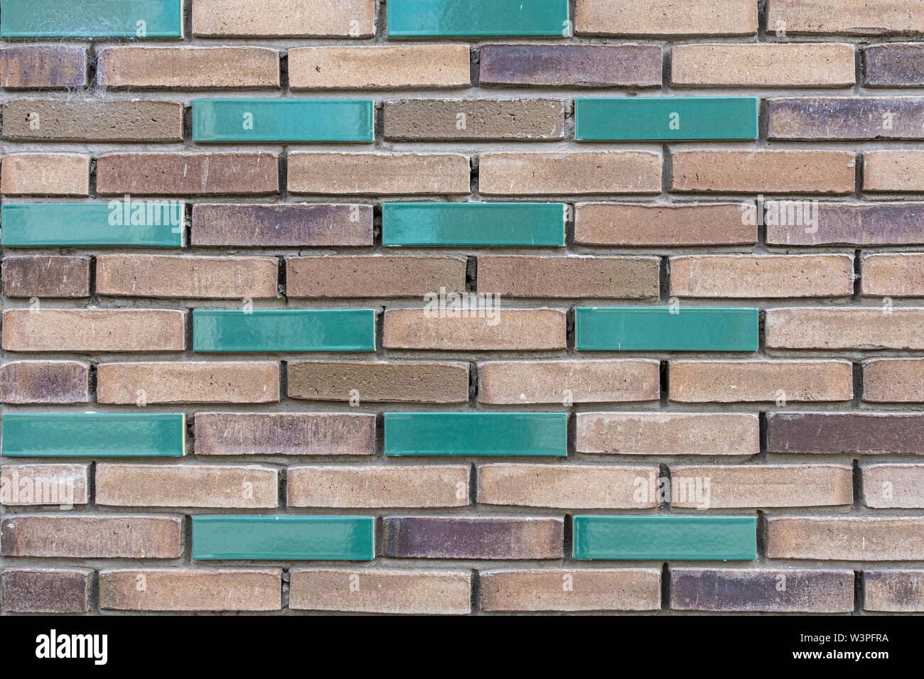 Marrone chiaro e scuro muro di mattoni con un paio di verde di mattoni colorati in esso Foto Stock