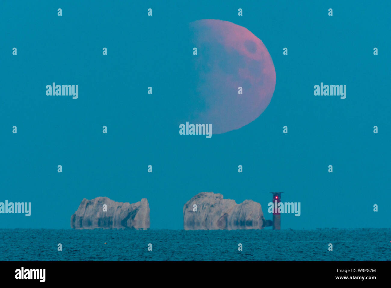 Gli aghi, Isle of Wight, Regno Unito. Il 16 luglio 2019. Regno Unito Meteo. Il parzialmente eclissato la luna piena sorge al di sopra degli aghi faro sull isola di Wight su una chiara serata. Le masse ombra è in colata attraverso una sezione di luna con il suo picco alle 22.30 quando 60% era in Eclipse. L'eclipse coincide anche con 50 anni poiché l uomo messo piede sulla luna. Credito Foto: Graham Hunt/Alamy Live News Foto Stock