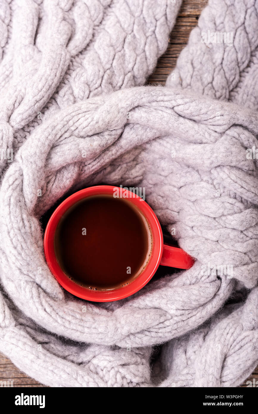 Un inverno sciarpa sul tavolo di legno esegue il wrapping di una tazza di tè o caffè. Foto Stock