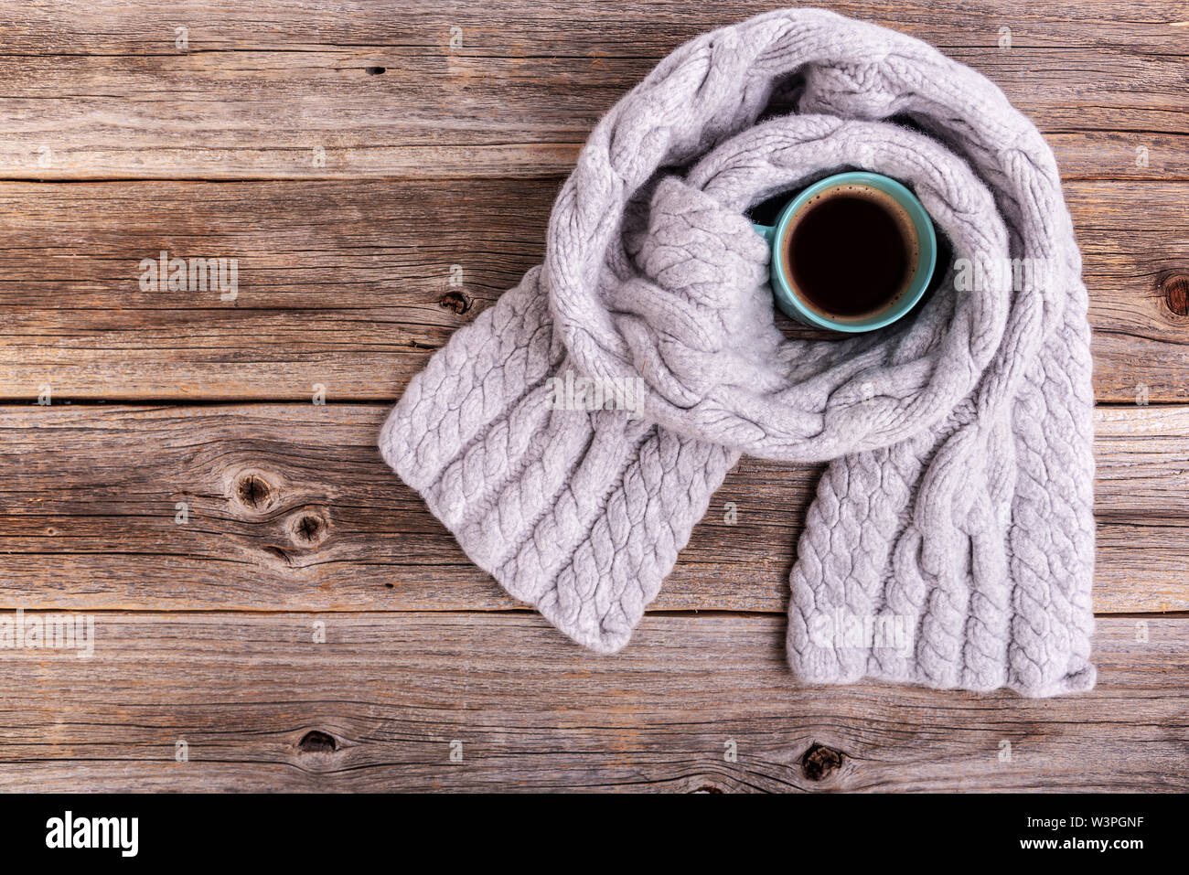 Un inverno sciarpa sul tavolo di legno esegue il wrapping di una tazza di tè o caffè. Foto Stock