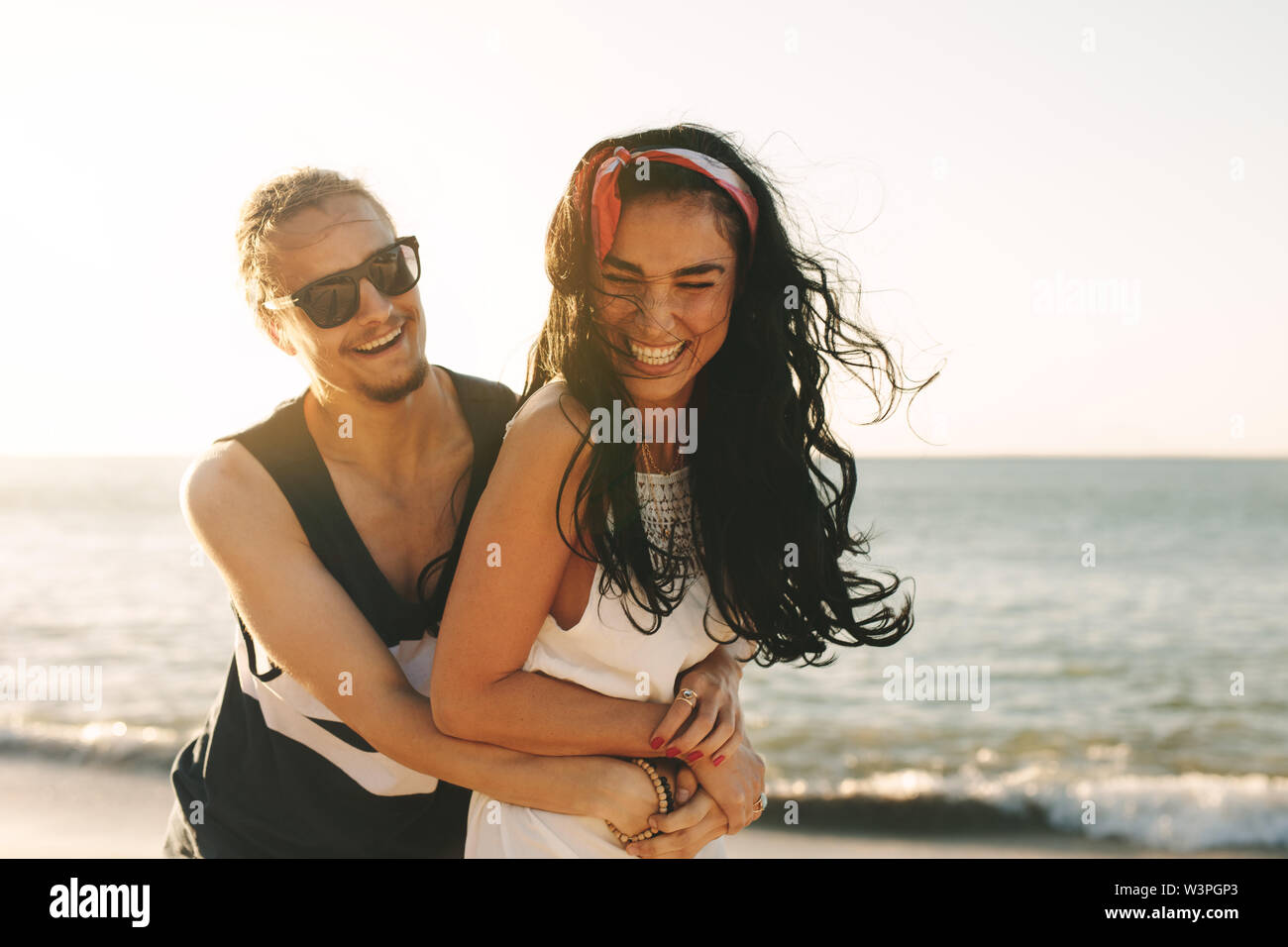 Coppia avente un grande momento insieme in estate spiaggia vacanza. Uomo con la sua ragazza da dietro e sorridente. Foto Stock