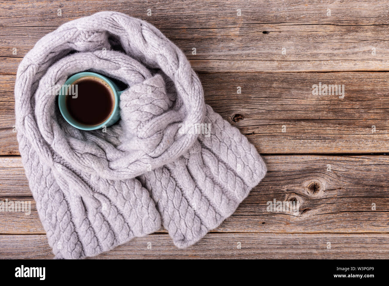 Un inverno sciarpa sul tavolo di legno esegue il wrapping di una tazza di tè o caffè. Foto Stock