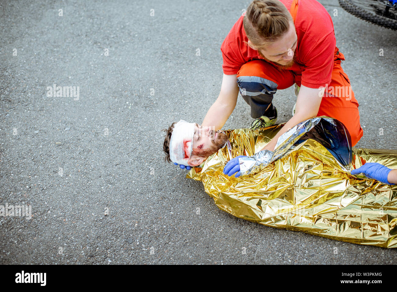 Lavoratore Ambluence copre uomo ferito con coperta termica, fornendo cure  di emergenza dopo l'incidente stradale Foto stock - Alamy