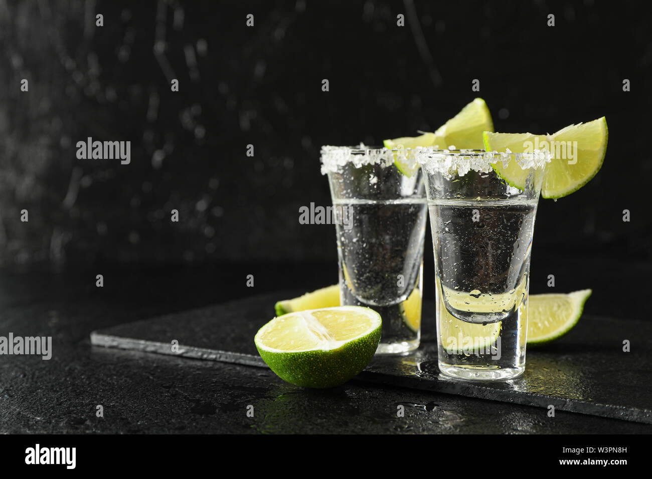 Scatti di Tequila con sale e fettine di lime sul nero sfondo umido Foto Stock
