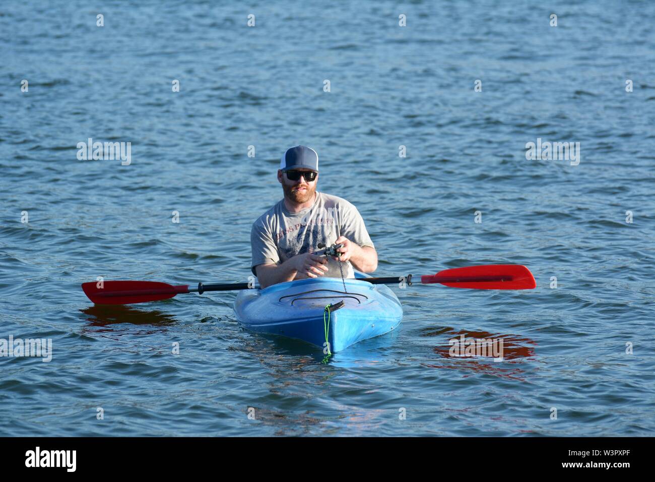 Un vero pescatore felice con catturato piccoli bassi sul suo colore blu kayak sul lago chiara Clearlake California USA America sulla tranquilla giornata di sole in estate da se stesso Foto Stock