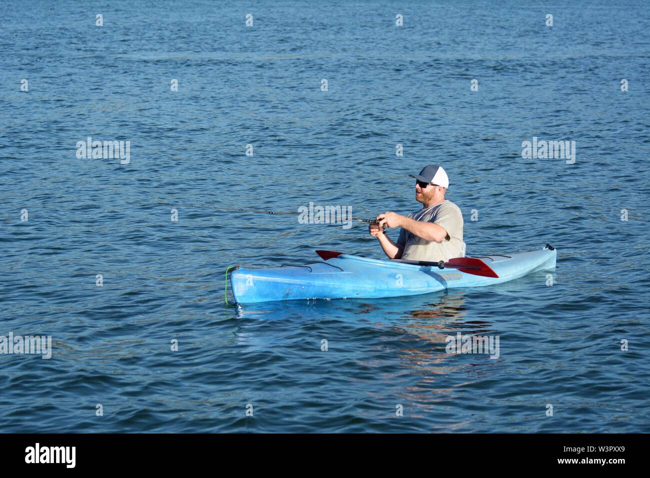Un vero pescatore felice con catturato piccoli bassi sul suo colore blu kayak sul lago chiara Clearlake California USA America sulla tranquilla giornata di sole in estate da se stesso Foto Stock