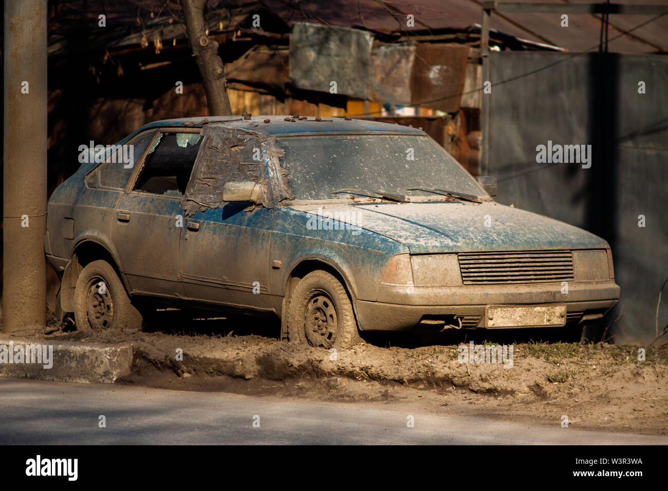 Vecchio e sporco auto abbandonate su sideroad con spesso strato di fango e di vetro rotto a luce diurna. Foto Stock