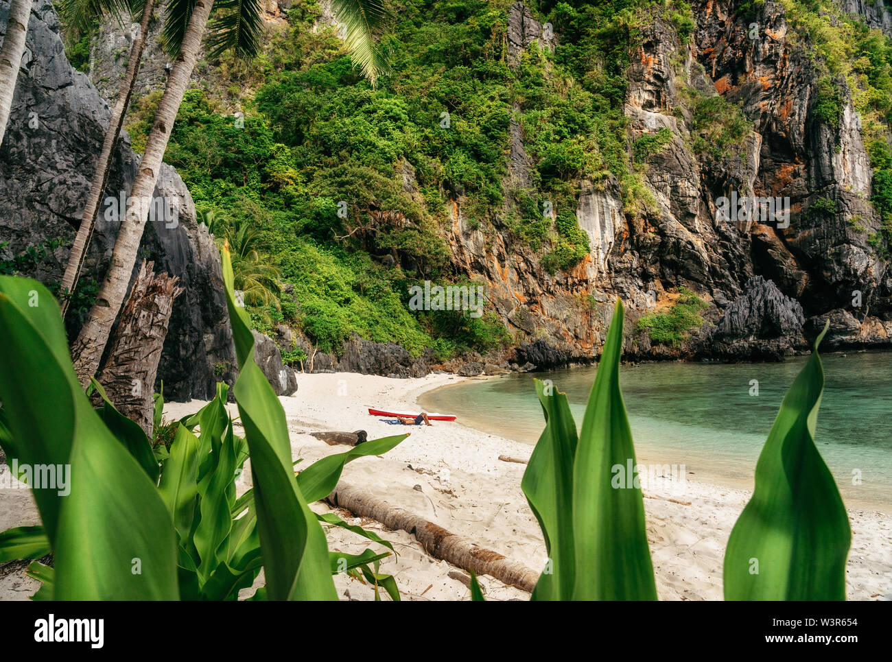 L uomo si rilassa sulla sabbia vicino al kayak sulla spiaggia di isola tropicale. El Nido, Filippine. Foto Stock