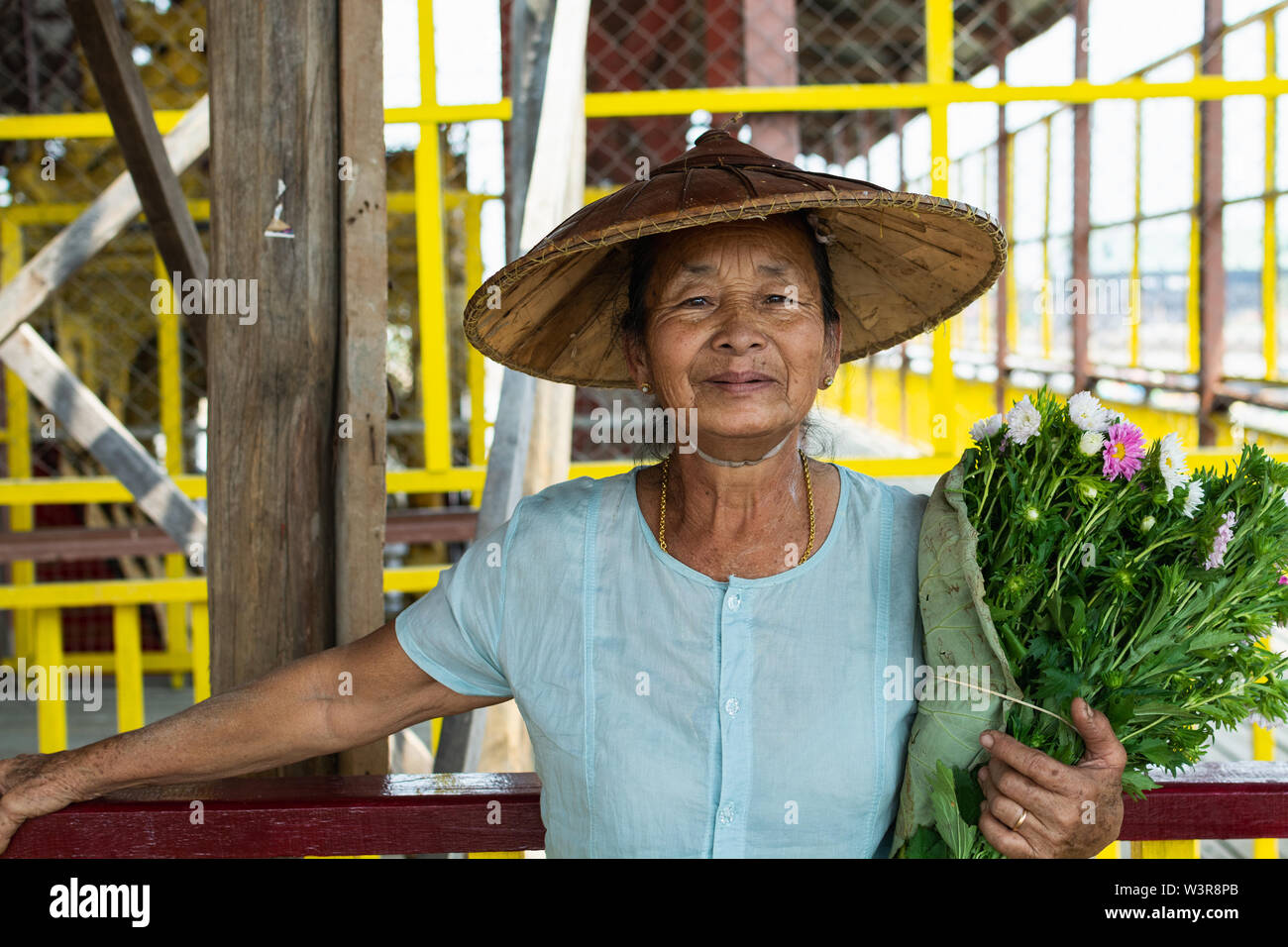 Maing Thauk, Myanmar - Aprile 2019: ritratto di un vecchio birmano donna sorridente in un cappello di bambù e fiori. Foto Stock