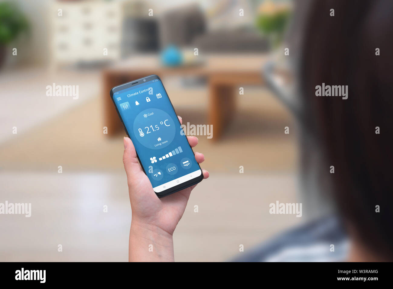 Donna utilizzare controllo climatico app su un telefono nella stanza vivente per la regolazione della temperatura e della ventilazione. Foto Stock