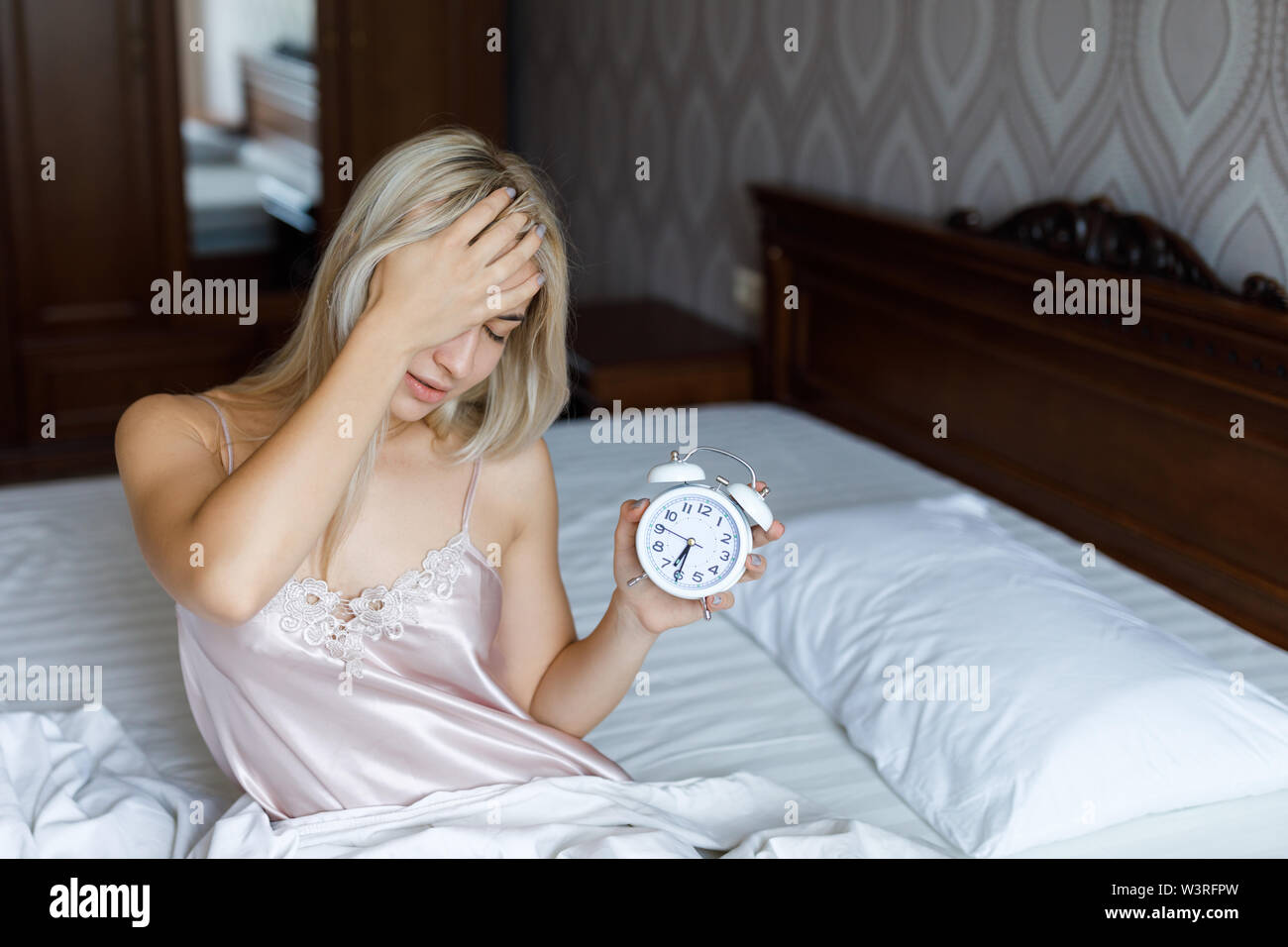 Bella giovane donna svegliarsi al mattino infastiditi sveglia tenendo la mano, il concetto di stile di vita. Foto Stock