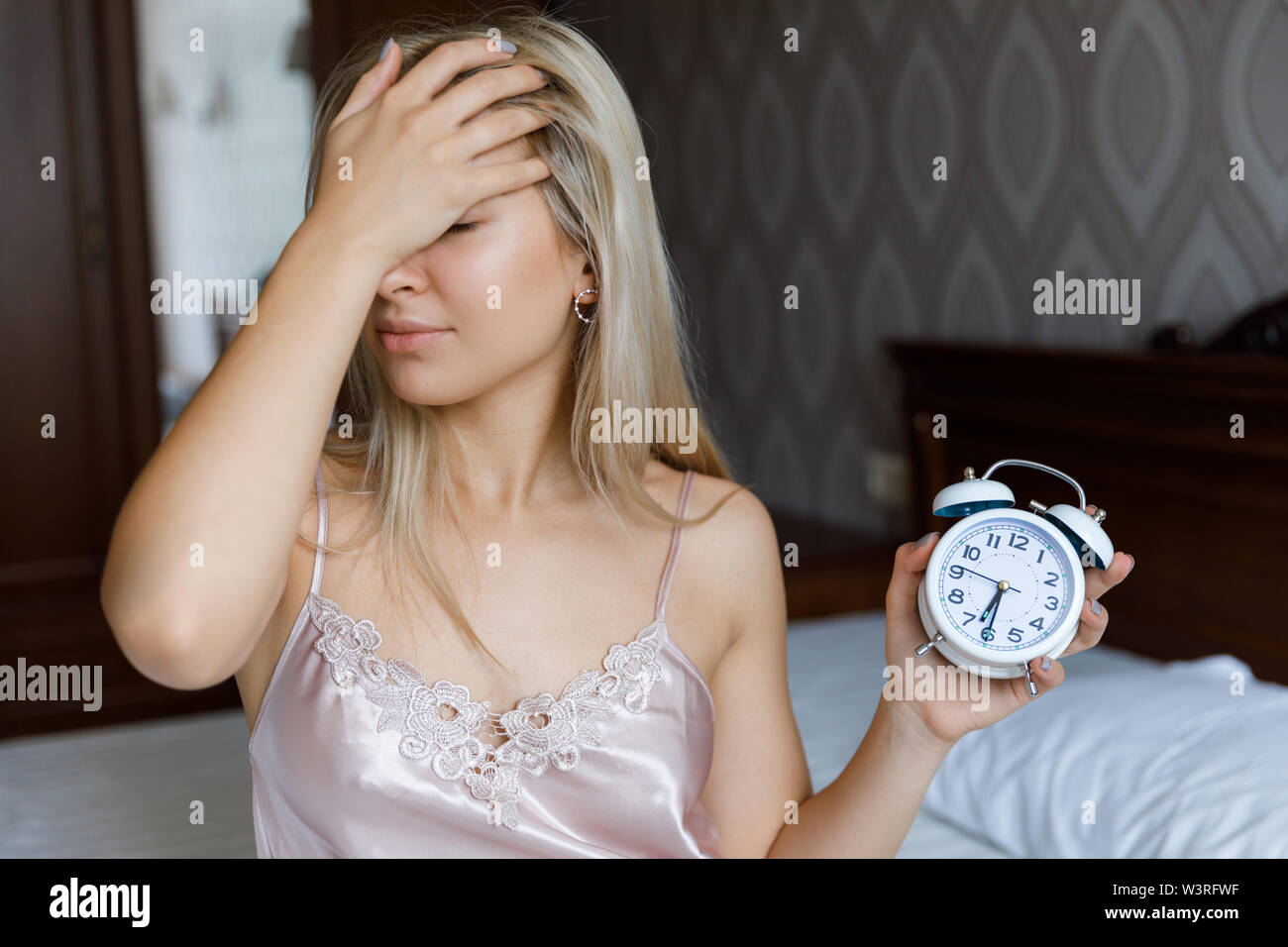 Bella giovane donna svegliarsi al mattino infastiditi sveglia tenendo la mano, il concetto di stile di vita. Foto Stock