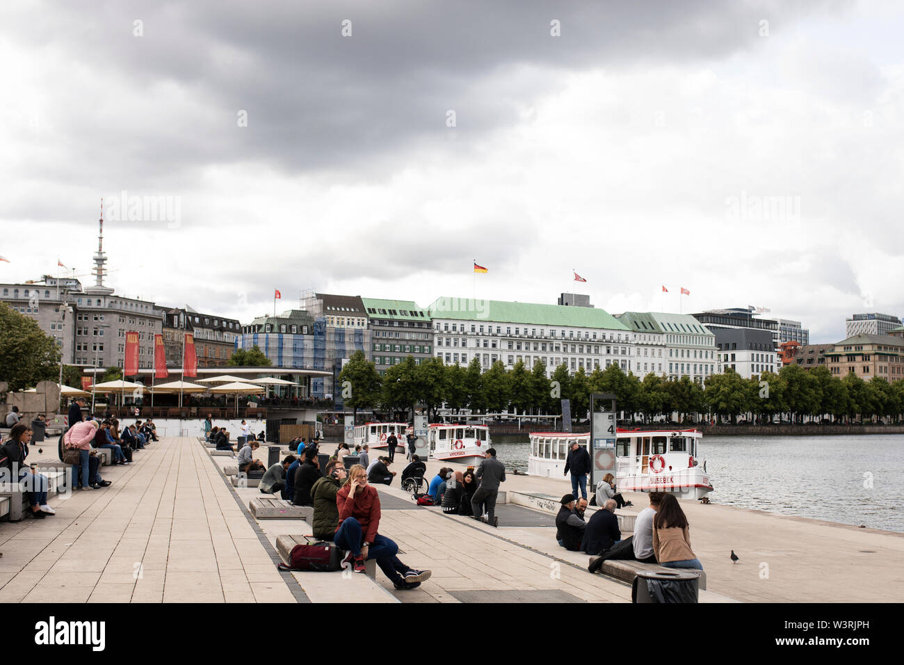 Le persone si riuniscono lungo il Binnenalster, un lago artificiale nel centro di Amburgo, in Germania, alimentato dal fiume Alster, dove attraccano le barche da tour sulla terrazza. Foto Stock