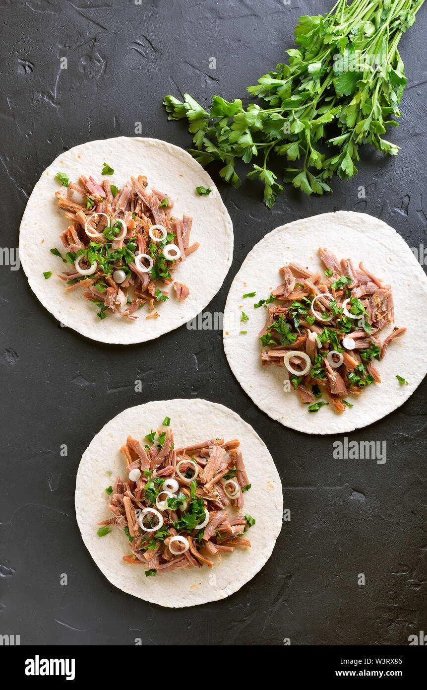 Tirate la carne di maiale soft tacos sulla pietra nera dello sfondo. Vista superiore, laici piatta Foto Stock