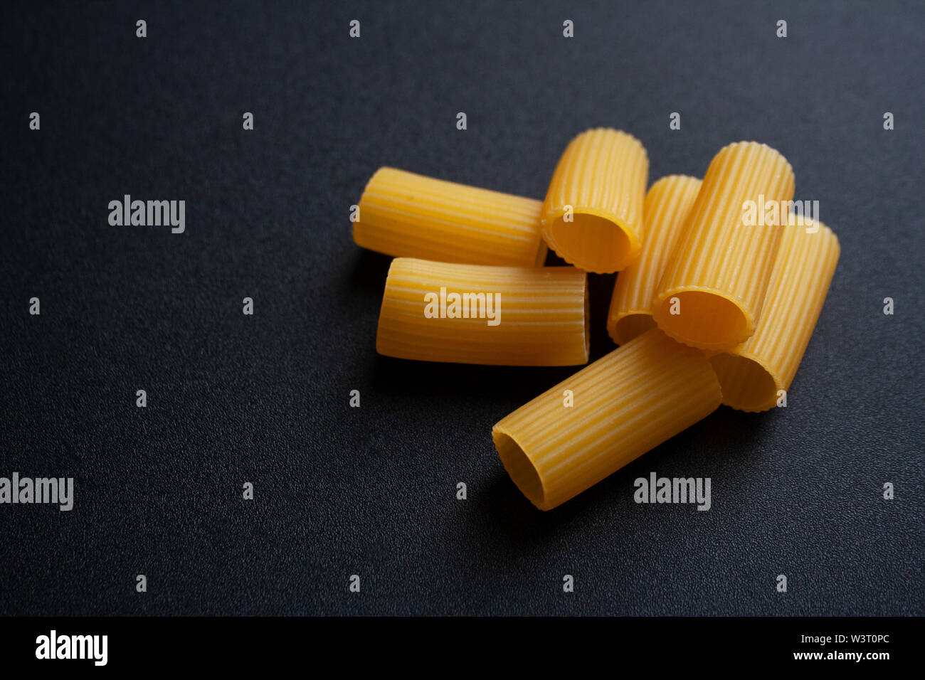 Raw tubo rigatoni pasta sagomata isolata su sfondo nero Foto Stock